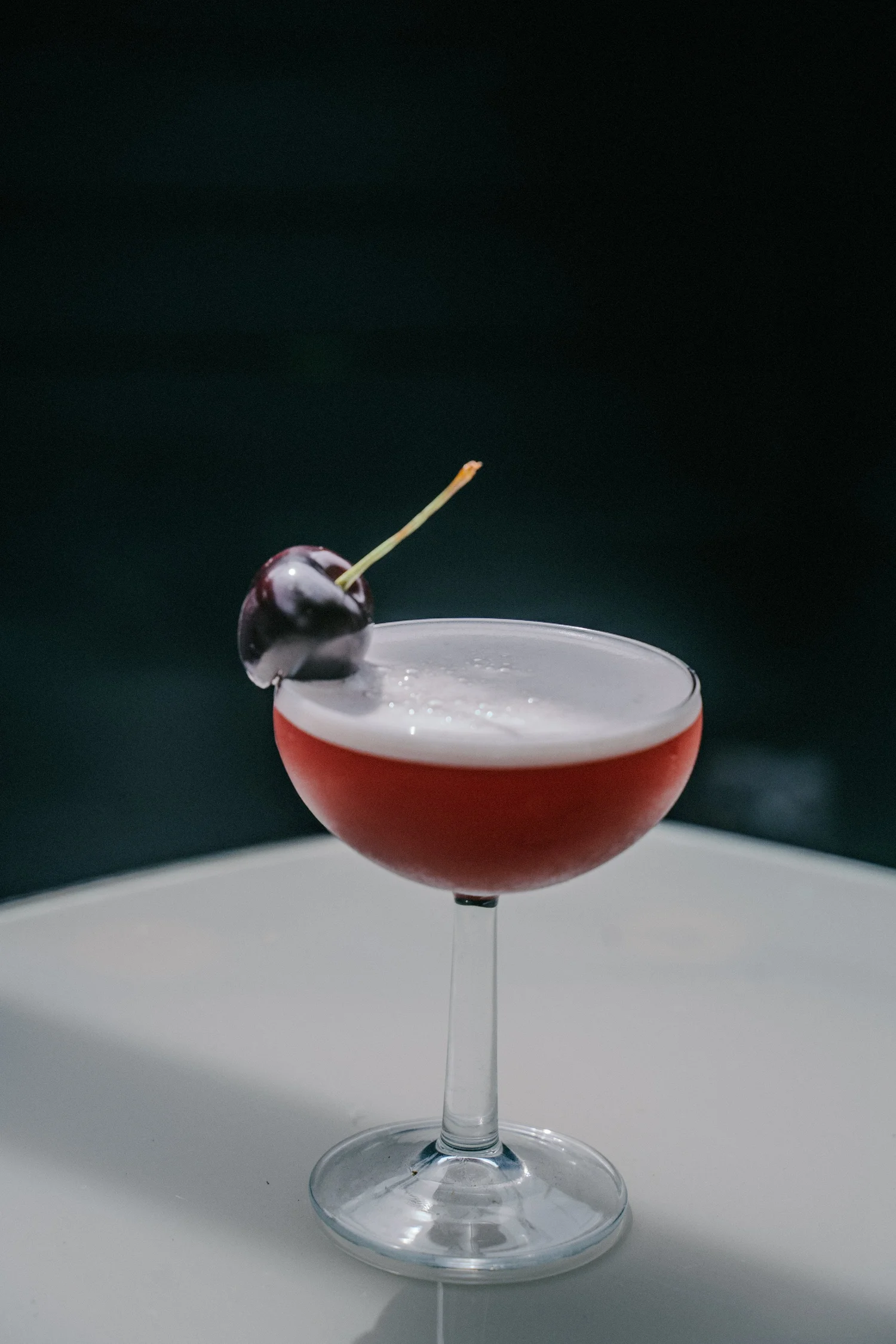 A cocktail served in a coupe glass with a cherry garnish.